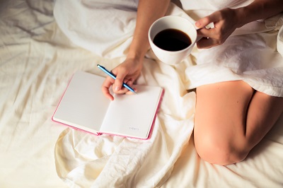 Woman sitting on bed with coffee writing in journal